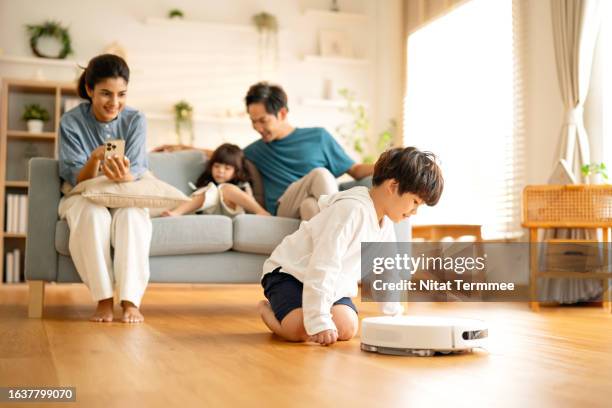 robot vacuums can simplify your cleaning process with smart features and apps. a boy is excited and having fun by crawling to follow a robot vacuum during auto cleaning on a parquet floor in the living room. - robot vacuum stock pictures, royalty-free photos & images