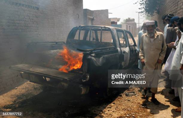Pakistani residents stand beside the burning wreckage of a car belonging to militant group Lashker-e-Islam during a security forces operation in...