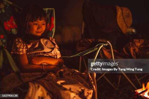 lovely cheerful girl enjoying the camp fire at dusk while having family camping trip in summer - innocent stock pictures, royalty-free photos & images