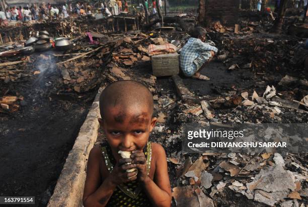 An young Indian slum dweller eats bread standing near gutted shanties in the Santoshpur area on the outskirts of Kolkata on March 16, 2013. Around...