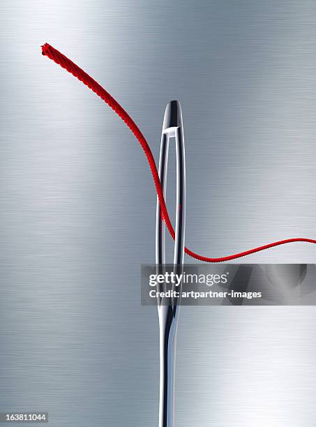 sewing needle with a red thread through the eye - exactitud fotografías e imágenes de stock