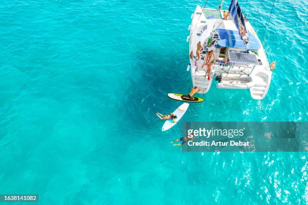 aerial view of a group of friends paddleboarding in the water sailing with catamaran on the formentera island in spain. - zonne eiland stockfoto's en -beelden
