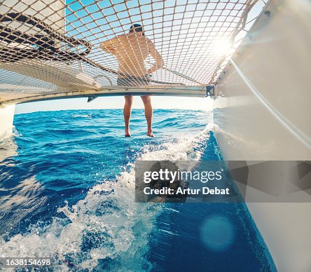 Creative angle of a man sitting on the catamaran bow sailing with the legs above the water in the middle of the Mediterranean sea. Creative angle of a man sitting on the catamaran bow sailing with the legs above the water in the middle of the Mediterranean sea.