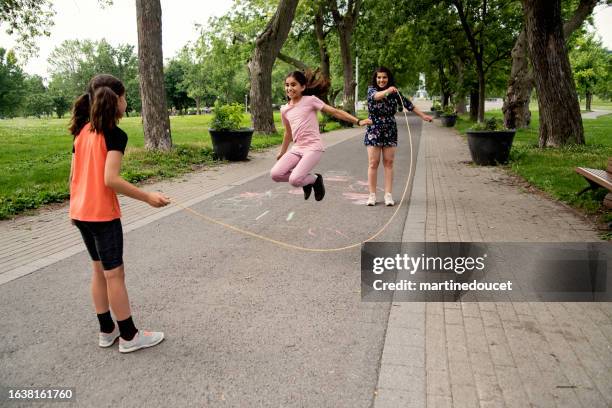 mother of middle-eastern ethnicity playing with two active daughters in park. - jump rope stock pictures, royalty-free photos & images