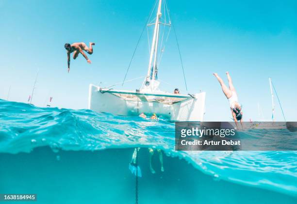 half underwater view of a couple jumping into water headlong in the paradise island of formentera sailing with a catamaran. - jumping of boat foto e immagini stock