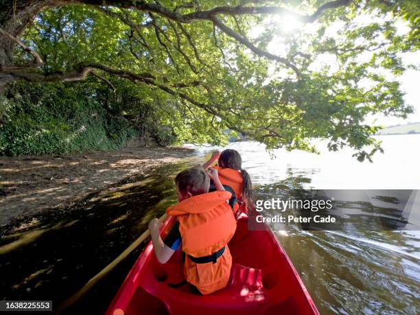 two children wearing life jackets paddling canoe on river - family red canoe stock pictures, royalty-free photos & images