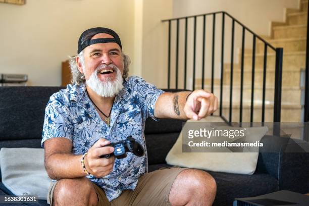 a 50 year old man looking like a happy badass enjoys playing video games in his living room - handsome 50 year old men imagens e fotografias de stock