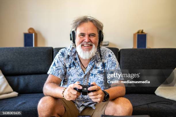 a 50 year old man looking like a happy badass enjoys playing video games in his living room - handsome 50 year old men imagens e fotografias de stock