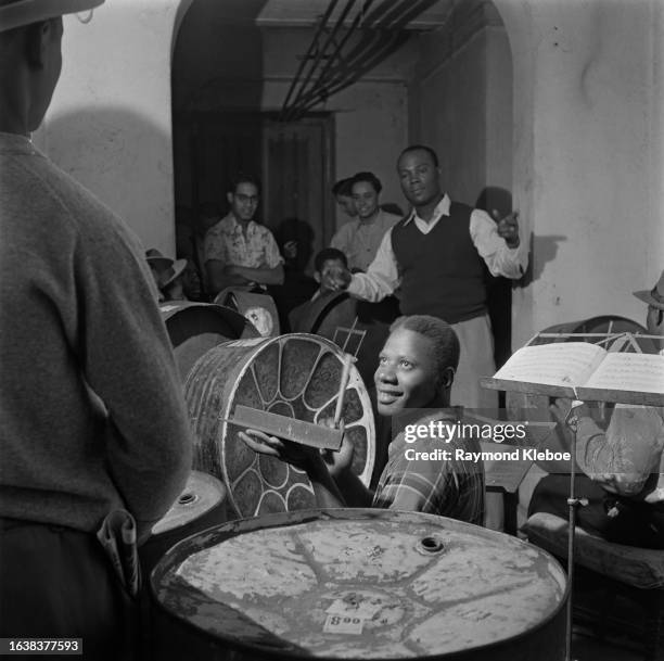 Man conducts a group of steel drum band musicians, January 1953. Original Publication: Picture Post - 6343 - Steel Drum Band - unpub. January 1953.