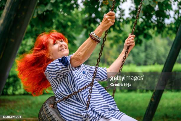 cheerful senior woman enjoying on a swing in a public park - senior colored hair stock pictures, royalty-free photos & images
