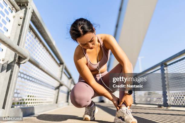mujer joven que tiene una lesión en la pierna al trotar, sentada en un puente - esguince fotografías e imágenes de stock