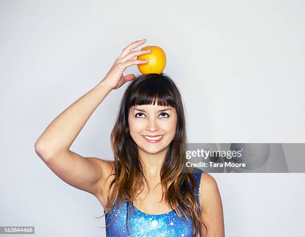 young woman balancing orange on top of head - carregar na cabeça - fotografias e filmes do acervo