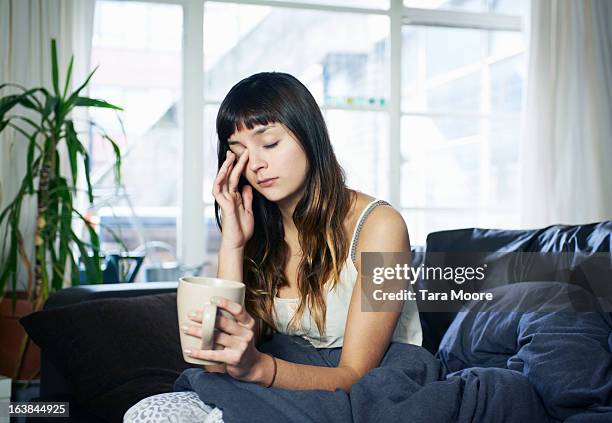 woman looking tired sitting on sofa - fatigué photos et images de collection