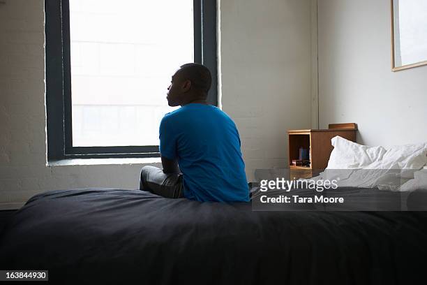 man sitting on bed - solitario foto e immagini stock