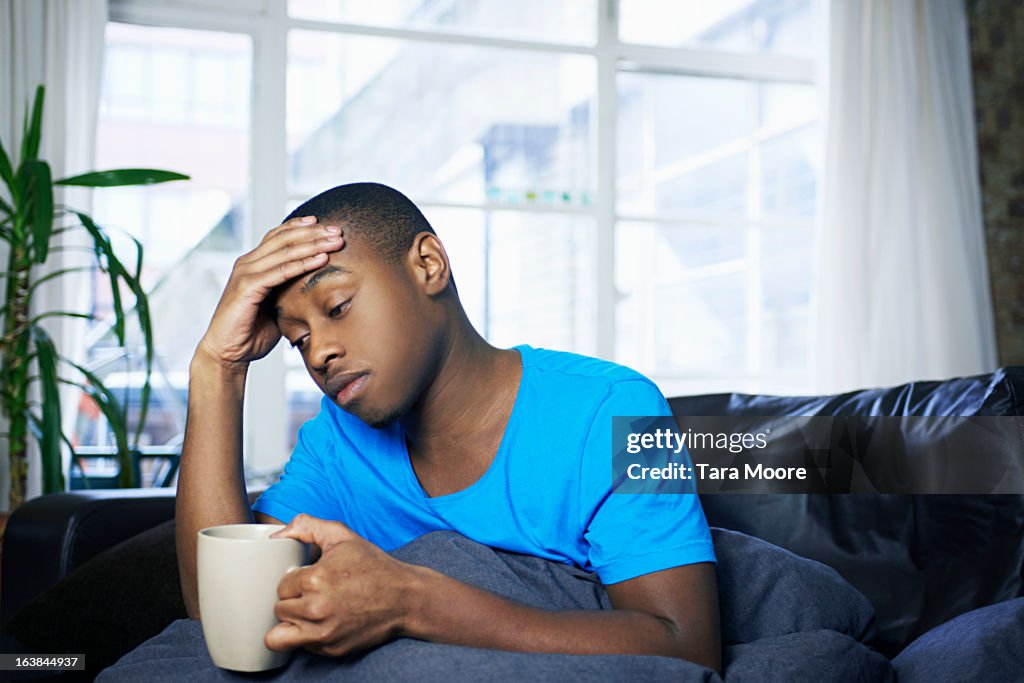 Young man sitting on sofa looking sick and tired