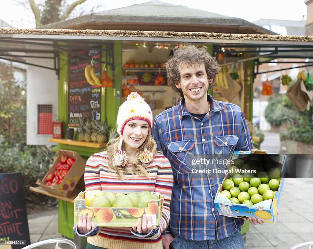 Couple holding fresh fruit in front of juice bar.