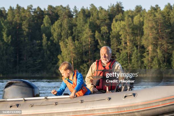 grandson with a bearded grandfather in life jackets in a motor boat during a weekend on the lake - buitenboordmotor stockfoto's en -beelden