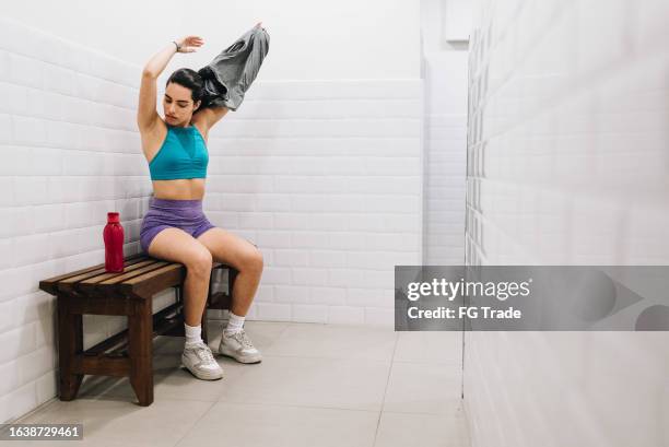 young woman taking off her shirt in the locker room at the gym - locker room stock pictures, royalty-free photos & images