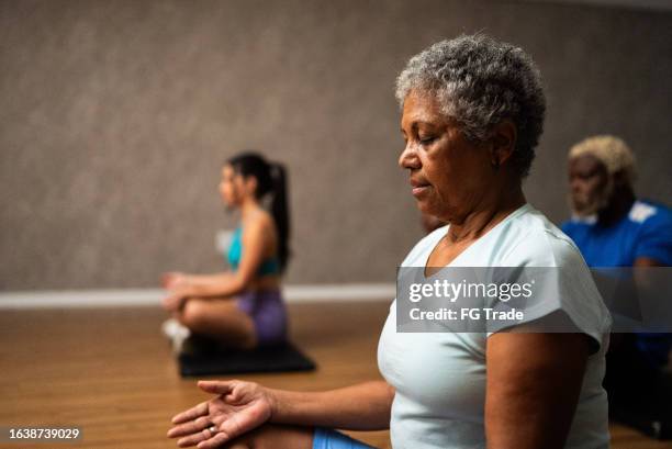 senior woman metitating at a gym - senior yoga lady stock pictures, royalty-free photos & images
