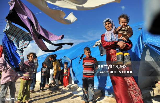Syrian woman carries her child outside their makeshift house at the refugee camp of Qah along the Turkish border in the village of Atme in the...