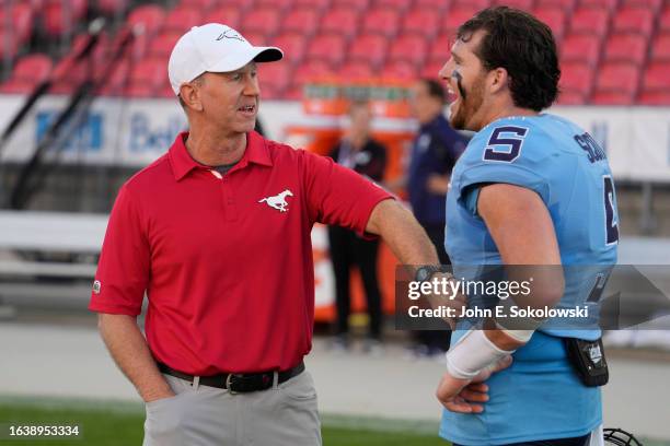 Head coach Dave Dickenson of the Calgary Stampeders talks with Bryan Scott of the Toronto Argonauts before a game at BMO Field on August 25, 2023 in...