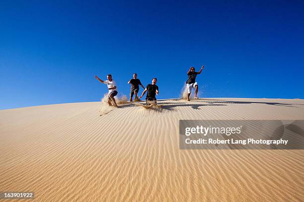 four people running down a sand dune having fun - desert dunes stock pictures, royalty-free photos & images