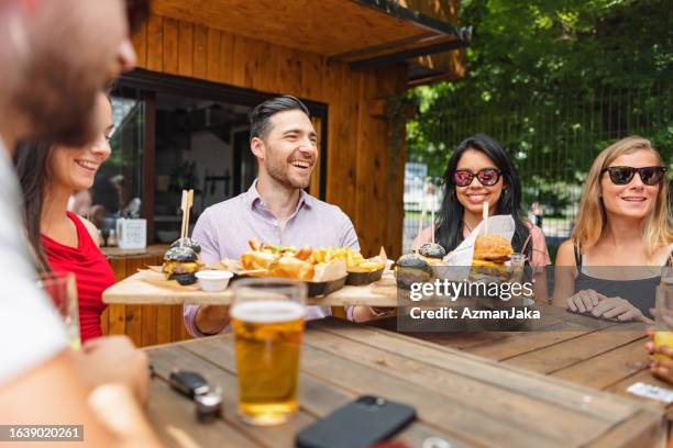 hombre caucásico feliz que trae un pedido de comida rápida a una mesa donde sus amigos están esperando - male burger eating fotografías e imágenes de stock