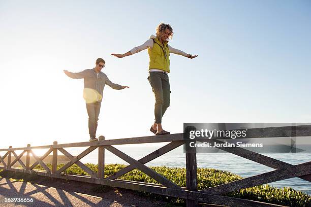 a couple balancing on a fence. - paralelo fotografías e imágenes de stock