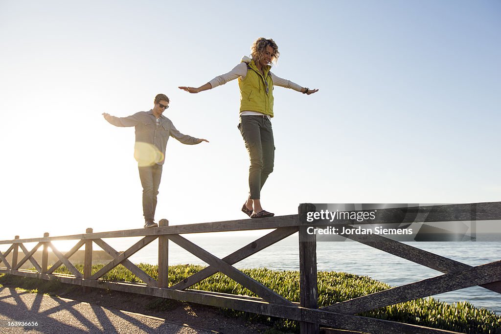 A couple balancing on a fence.