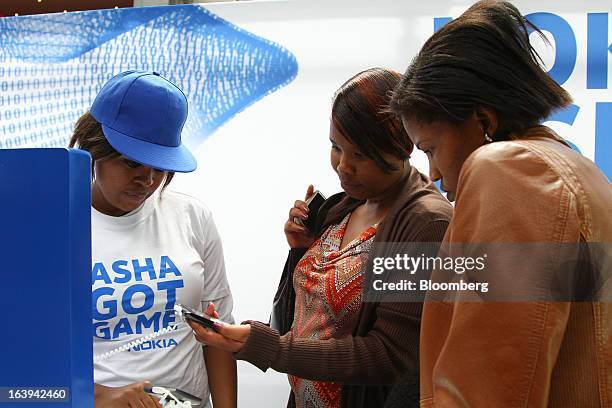 An employee shows shoppers new Nokia Asha smartphones during a promotional "activation day" event by Nokia Oyj in Maponya Mall in Soweto, South...