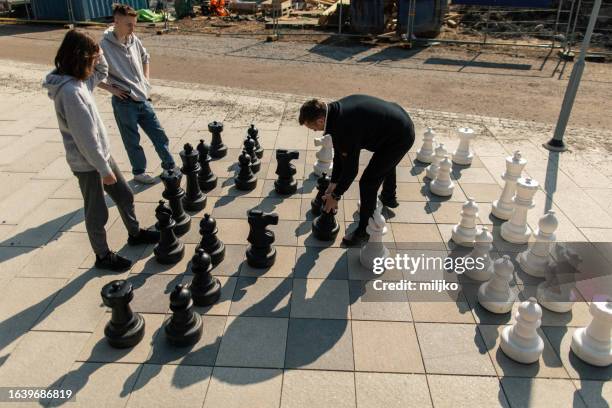 two teenage boys playing chess against man in city park - chessmen stock pictures, royalty-free photos & images