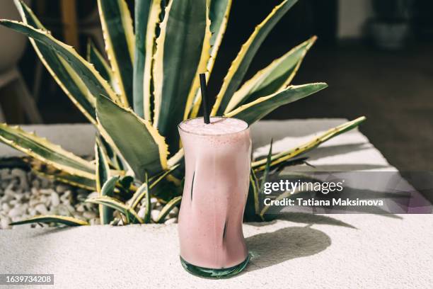 pink strawberry smoothie on green plant background in outdoor café, sunny day. - milk plant stock-fotos und bilder