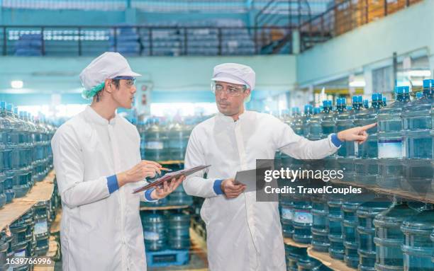 two worker scientist with laboratory inspect quality of drinking water inside of the production line factory while using digital tablet to check cleanliness and standard. quality assurance - bottling plant stock pictures, royalty-free photos & images