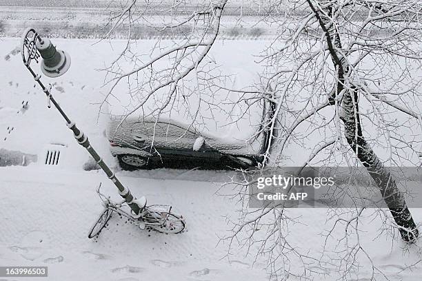 Bicycle and a car are coverd by snow during a snowfall in Berlin, on March 19, 2013. AFP PHOTO / ISABELLE WIRTH