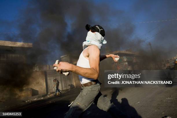 Masked Palestinian youths hurl stones at Israeli forces during clashes on October 5, 2009 in the east Jerusalem Shuafat refugee camp. Police flooded...