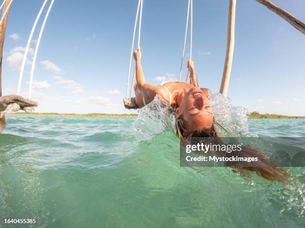 junge frau, die sich an einem sonnigen tag auf schaukel über einer schönen lagune amüsiert - schaukel frau stock-fotos und bilder