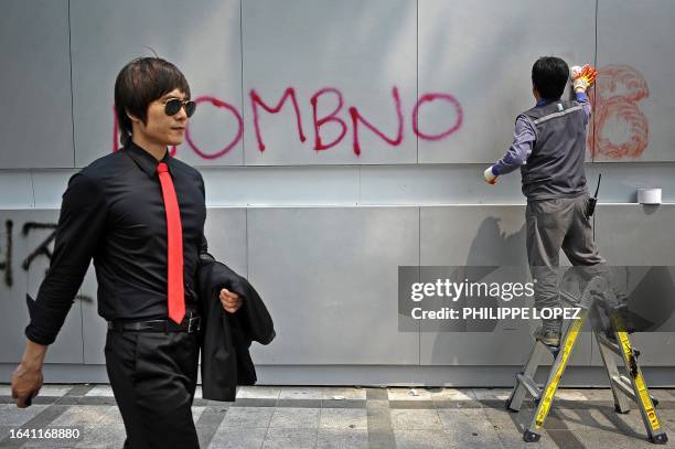 Pedestrian walks past a worker removing anti-government slogans reading "No MB" from a wall, in reference to the name of the current president Lee...