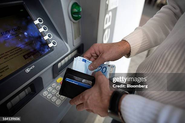 Man places euro banknotes in his wallet after withdrawing them from an automated teller machine operated by Laiki Bank, also known as Cyprus Popular...