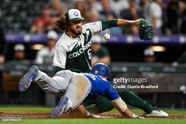 Davis Schneider of the Toronto Blue Jays scores a ninth inning run after a wild pitch and a missed tag attempt by Justin Lawrence of the Colorado...