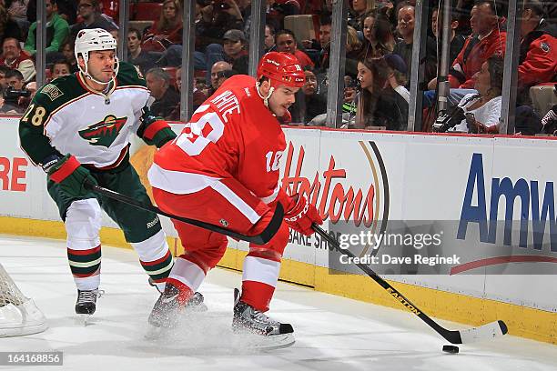 Ian White of the Detroit Red Wings handles the puck as Zenon Konopka of the Minnesota Wild pressures him during a NHL game at Joe Louis Arena on...