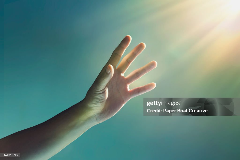 Hand reaching towards glowing light from corner