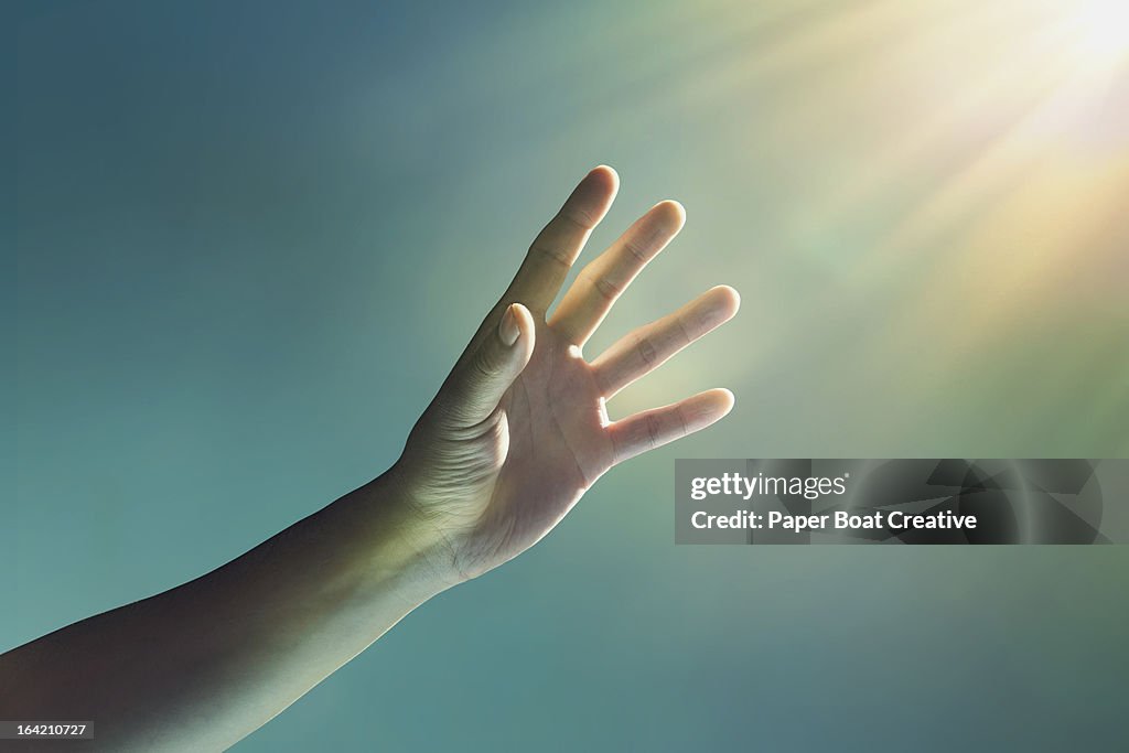 Hand reaching towards glowing light from corner