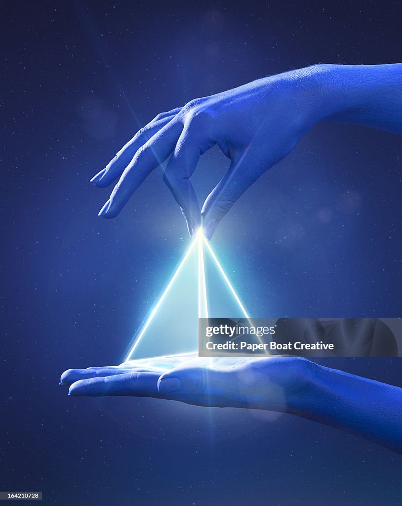 Blue painted hand pinching a glowing light prism