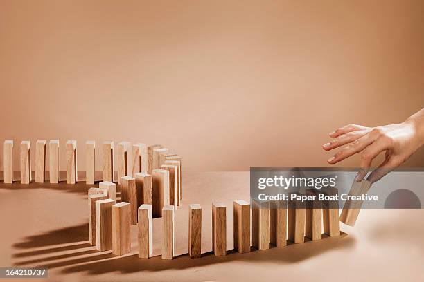 hand about to knock over dominoes made out of wood - dominos photos et images de collection