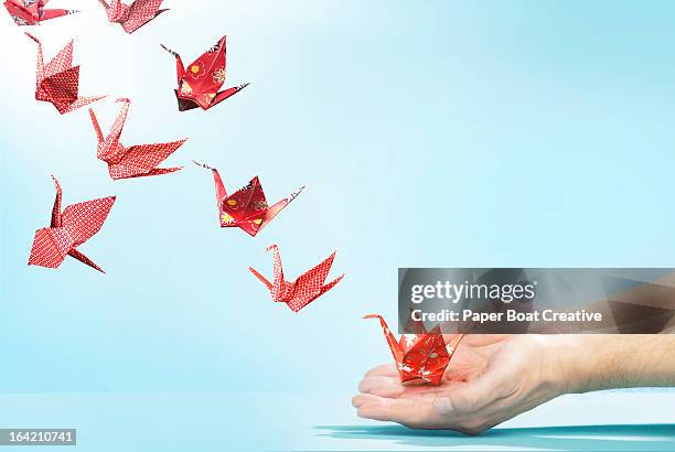 red origami cranes flying away from hands - crane bird stock-fotos und bilder