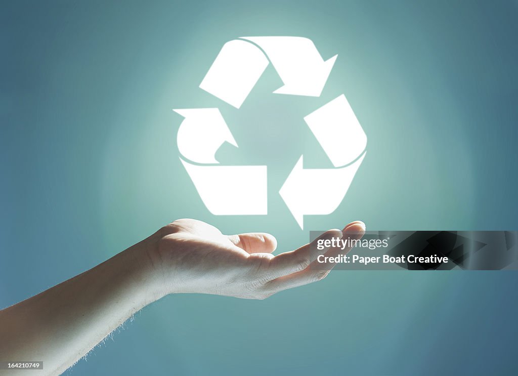 Glowing recycling sign floating above hand