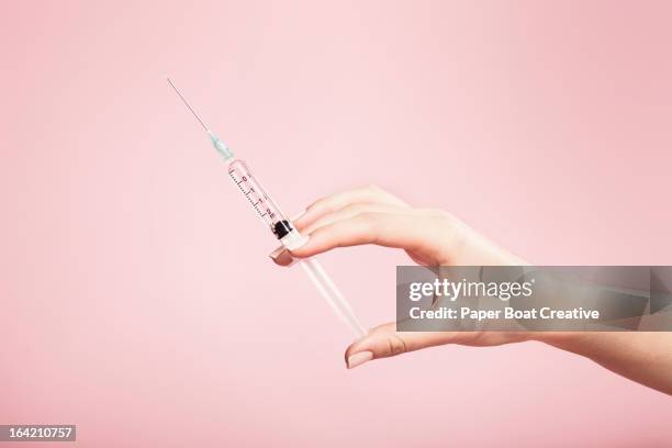 hand holding syringe in plain pink background - needle fotografías e imágenes de stock