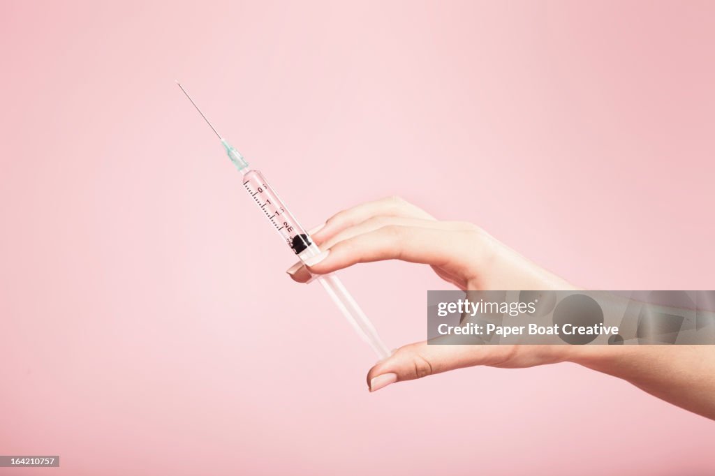 Hand holding syringe in plain pink background