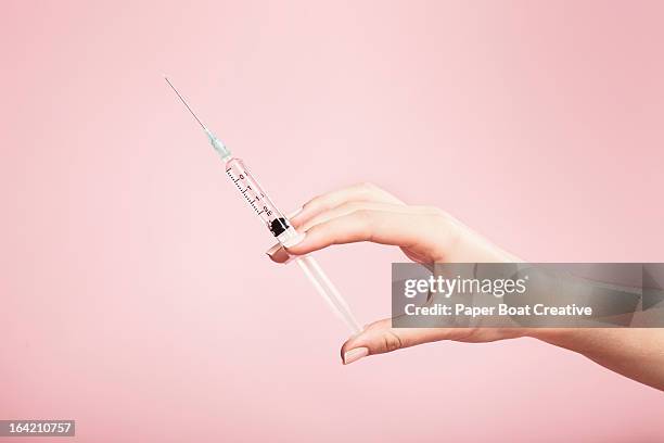 hand holding syringe in plain pink background - woman portrait studio shot stock pictures, royalty-free photos & images