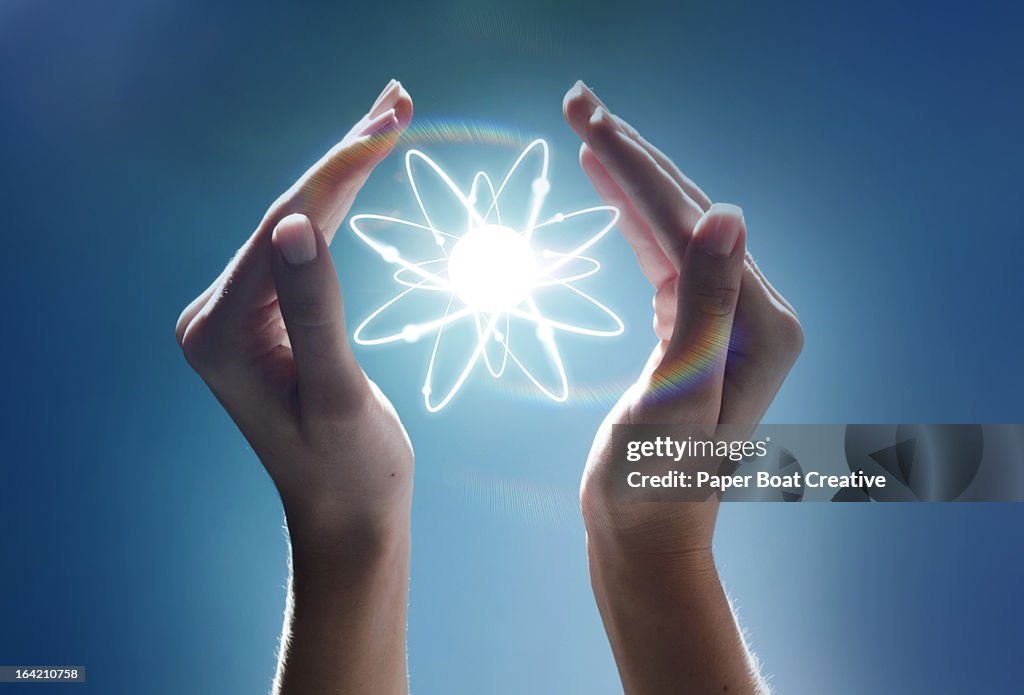 Hands cupping a glowing atom in the studio